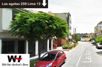 a red car parked on a street next to a tree at White Hope Apartment in Lima