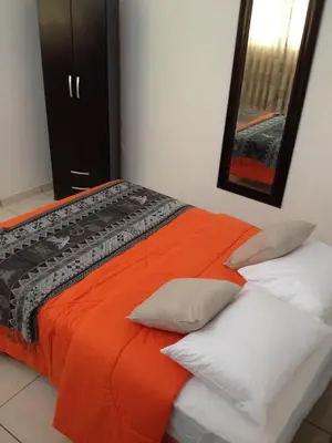 a bedroom with a bed with an orange blanket and pillows at La Maison de Lydia in Nazca