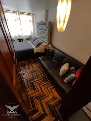 a living room with a black leather couch and a window at Casita Libertad Chorrillos in Lima