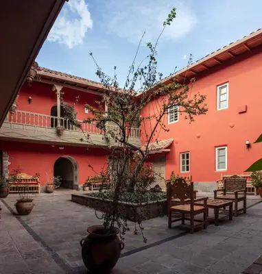 a red building with benches and a tree in the courtyard at Tambo del Arriero Hotel Boutique in Cusco