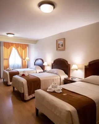 a hotel room with three beds and a window at Hotel Britania San Borja in Lima