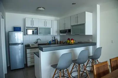 a kitchen with white cabinets and a counter with bar stools at Condominio Nuevo Paracas in Paracas