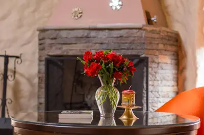 a vase with red flowers on a table in front of a fireplace at Intiterra Apart Hotel Villas in Urubamba