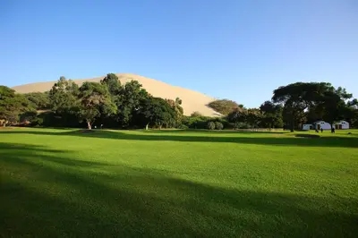 a large field of grass with a sand hill in the background at Hotel Las Dunas in Ica
