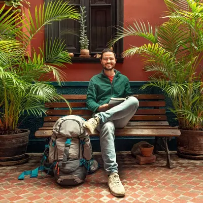 a man sitting on a bench with a book and a backpack at KACLLA, The Healing Dog Hostel in Lima
