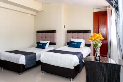 a bedroom with two beds and a table with a vase of flowers at Hotel Luna de Oro Cusco in Cusco