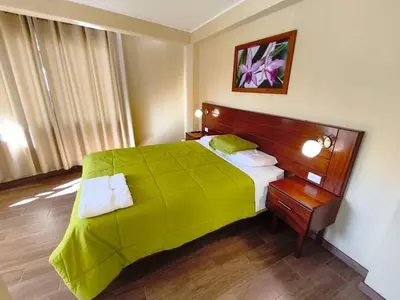 a bedroom with a large bed with a green blanket at Hospedaje Cattleya in Oxapampa