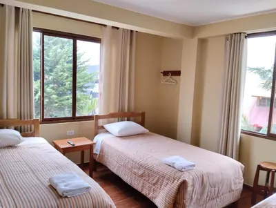 two beds in a room with two windows at Hospedaje Cattleya in Oxapampa