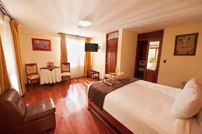 a bedroom with a bed and a table and a chair at Hotel Mabey Urubamba in Urubamba