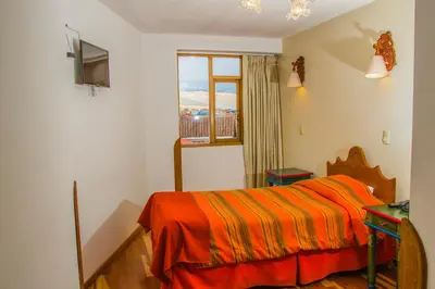 a bedroom with a bed with an orange blanket and a window at Hotel Warari in Cusco