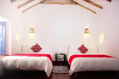 two beds in a room with white walls and red sheets at Rumi Wasi in Cusco