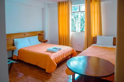 a room with two beds and a table and a window at La Posada D'Benjamín in Oxapampa