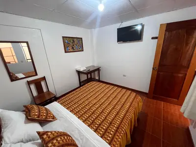 a bedroom with two beds and a television on the wall at Hospedaje Familiar Laos in Oxapampa
