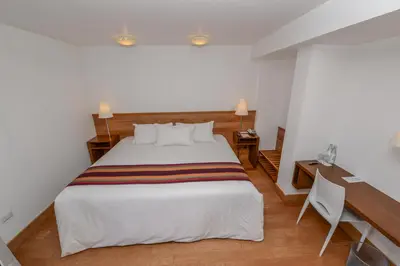 a bedroom with a large white bed and a desk at Hotel Plaza de Armas Cusco in Cusco