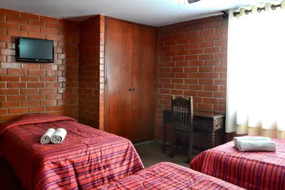 a bedroom with two beds and a tv on a brick wall at Hotel Esperanza in Lima