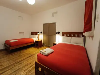 a room with two beds with red sheets and wooden floors at Pariwana Hostel Cusco in Cusco