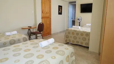 a room with two beds and a table and a mirror at Hotel Las Flores in Ica