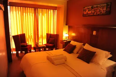 a bedroom with a large bed with two chairs and a window at Hotel Waynapicchu in Cusco