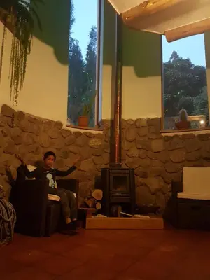a man sitting in a chair in a living room with a wood stove at Mágico lugar en el Valle Sagrado in Cusco