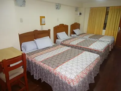 three beds in a room with a wooden table and a table at Hotel Panamericano in Lima