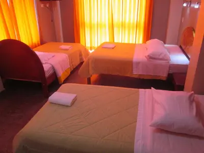 a hotel room with three beds and a chair at Hotel Villa Santa Ana in Quillabamba