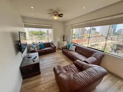 a living room with leather couches and a large window at Céntrico Apartamento Parque Kennedy Miraflores in Lima