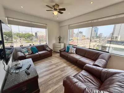 a living room with leather couches and large windows at Céntrico Apartamento Parque Kennedy Miraflores in Lima