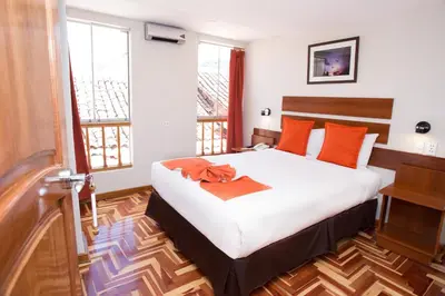 a bedroom with a bed with orange pillows and a desk at Hotel Arcangel in Cusco