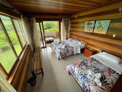 two beds in a room with wooden walls and windows at Mercedes Lodge in San Ramón
