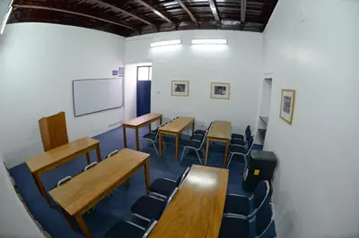 a classroom with desks and chairs and a white wall at La Casa de Fray Bartolome in Cusco