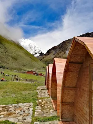 a couple of small buildings in a field with a mountain at Soraypampa Hostel - Private Cabins & Dorms for Self-Guided Humantay & Salkantay Trek -Comidas-hot shower-wifi-Pack horses in Salcantay