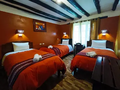 a room with three beds with orange sheets at Wayras Hostal in Ollantaytambo