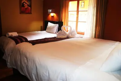 a bedroom with two beds with white sheets and a window at Wayras Hostal in Ollantaytambo