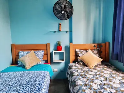 a blue bedroom with two beds and a fan at EL TUMI - Aeropuerto in Lima