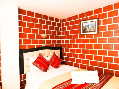 a brick walled bedroom with a bed with red pillows at Hostal Encanto Machupicchu in Machu Picchu