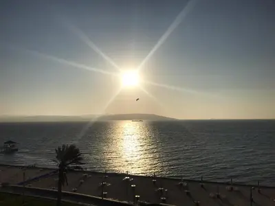 a bird flying over the ocean with the sun in the sky at Paracas top tower beach front in Paracas