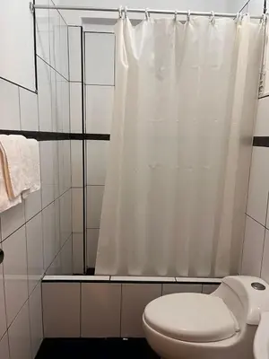 a bathroom with a white shower curtain and a toilet at Hotel Munay in Paracas