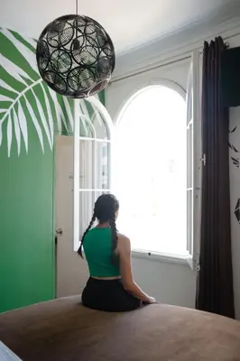 a woman sitting on a bed looking out a window at The Secret Garden Hostel in Lima