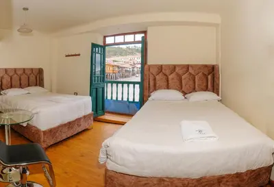 a bedroom with two beds and a table and a window at Hostal Chasky in Cusco