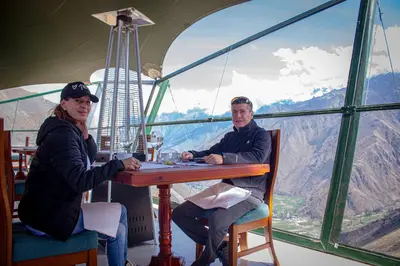 a man and a woman sitting at a table in front of a window at Vertical Sky Suites in Ollantaytambo
