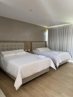 two beds in a bedroom with white sheets at Hotel El Condor in Paracas