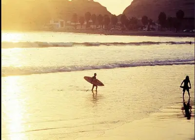 two people walking on the beach with a surfboard at IntiPunku in Cerro Azul