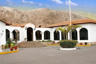 a large white building with a mountain in the background at VPX Hoteles Cieneguilla in Cieneguilla