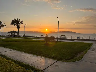 a sunset over the ocean with palm trees and a sidewalk at Suite 1 Fila Vista Bahía Paracas- La Velas 601 T1 in Paracas