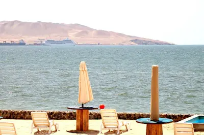 two chairs and umbrellas on the beach with a cruise ship at Casa 33 Sotavento Paracas in Paracas