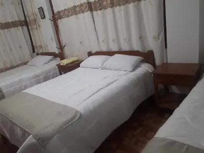 two beds in a room with two tables and a bed sidx sidx sidx at Hospedaje Olguita in Oxapampa