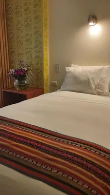a bed with a white pillow and a vase of flowers at Hotel Pucara Machupicchu in Machu Picchu