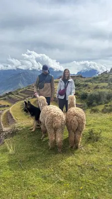 two people and a dog standing on a hill with sheep at Sky Dome Peru in Cusco